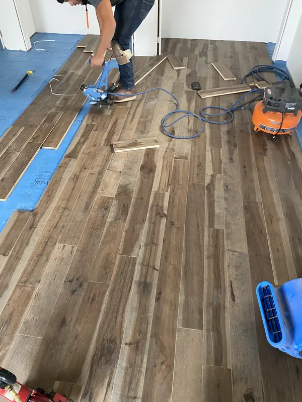 Boards going down over blue underlayment with the nailer still in shot